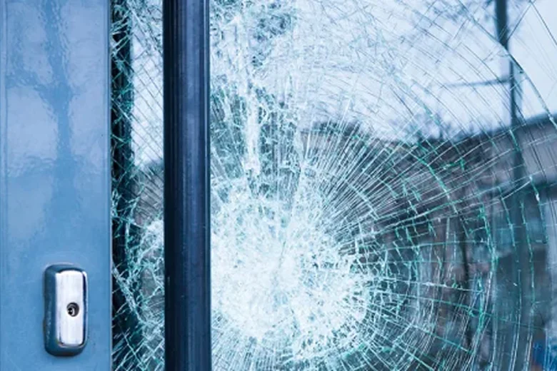 Close-up of a shattered glass door with spiderweb cracks radiating from a central impact point.