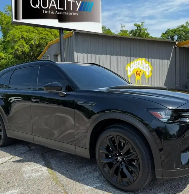 Shiny black SUV with dark tinted windows parked in front of a shop with a "Quality Tint & Accessories" sign and a mural reading "UnderWraps Tint."