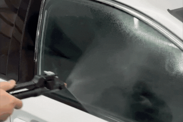 As part of the Understanding Window Tinting process, a person uses a heat gun to apply tint film onto a car window, ensuring it adheres smoothly without bubbles. The film darkens the glass for added privacy and UV protection.