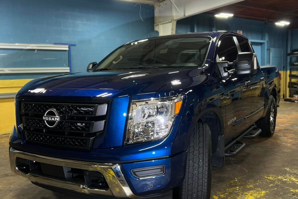 A dark blue Nissan Titan with freshly tinted windows parked indoors under bright lighting, showcasing a professional tint job that complies with legal tint in Mississippi. The front side windows appear sleek while maintaining the 28% visible light transmission required by state law.