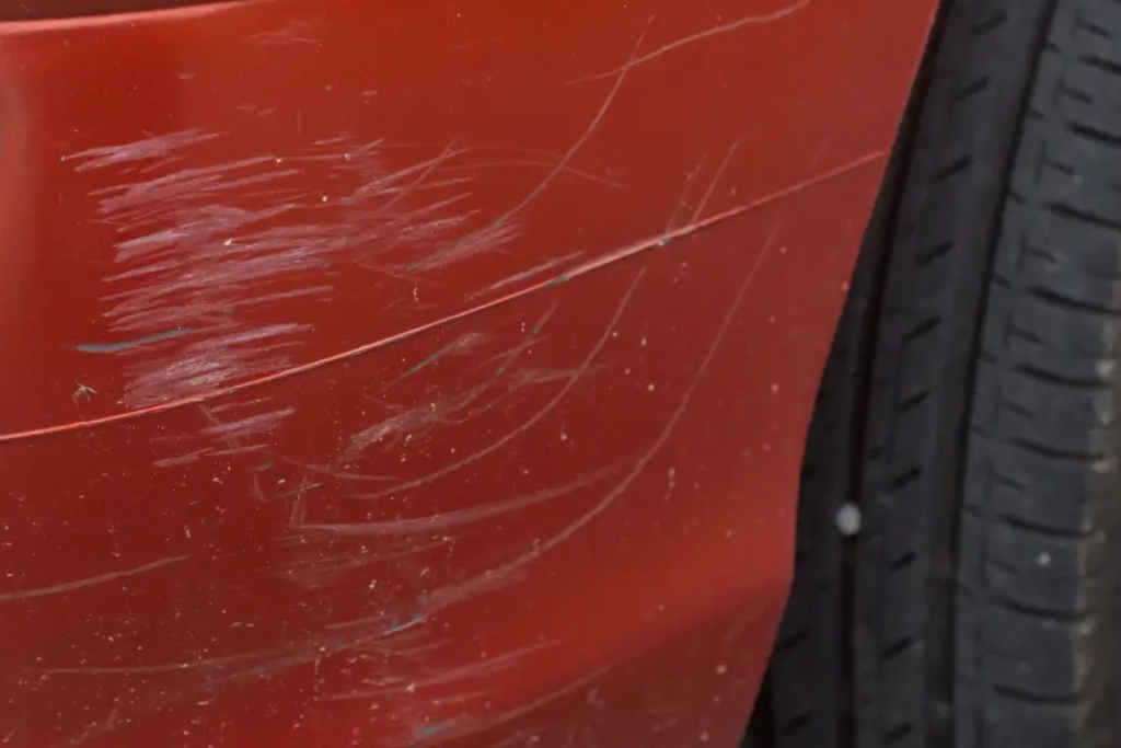 Close-up of a red car's bumper with visible scratches near the rear tire, showing the type of paint damage that ceramic coating doesn't prevent, aligning with the topic ceramic coating doesn't do.
