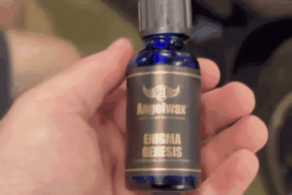 Close-up of a hand holding a bottle of Angelwax Enigma Genesis ceramic coating, a high-end nano-ceramic product used to protect vehicle paint with long-lasting, hydrophobic and UV-resistant properties, supporting the topic of What Is Ceramic Coating.