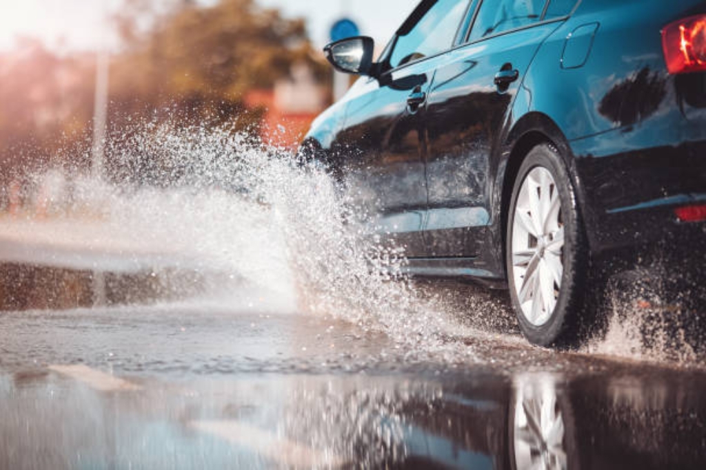 A sleek black car splashes through a wet road in Gulfport, highlighting the hydrophobic effect of ceramic coating that repels water and grime, supporting the topic What Is Ceramic Coating.
