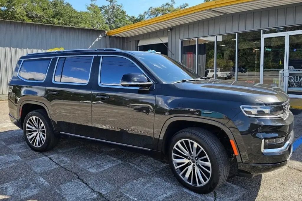 Black SUV with freshly installed window tint parked outside Quality Tint & Accessories shop.