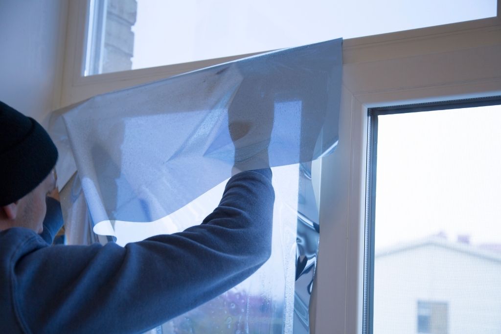 Professional installer applying a blue-tinted film to a window for improved energy efficiency and privacy.