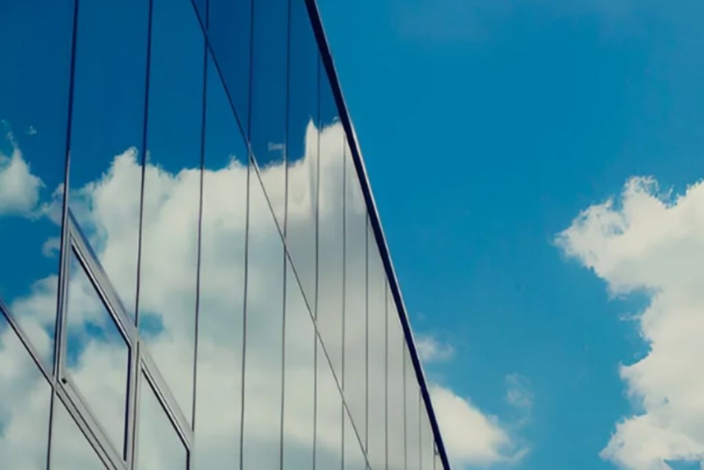 Glass windows of a modern commercial building reflecting the blue sky and white clouds.