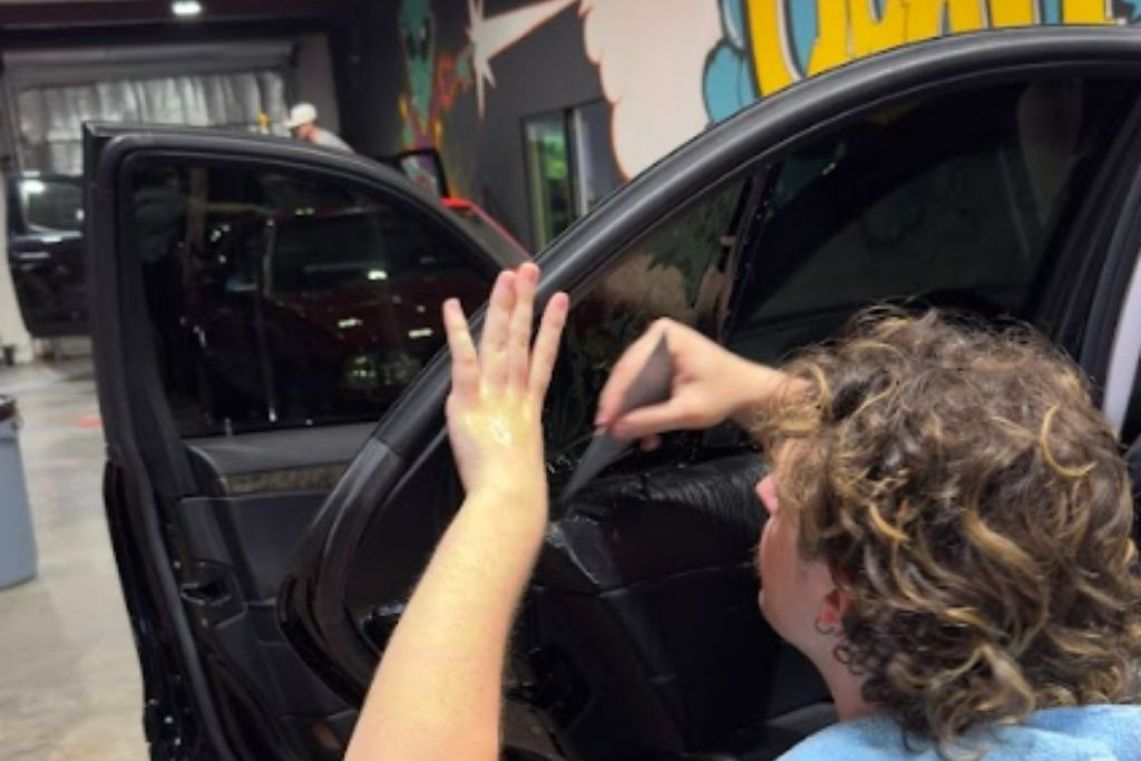 Quality Tint & Accessories expert installing window tint film on a car door inside the workshop.