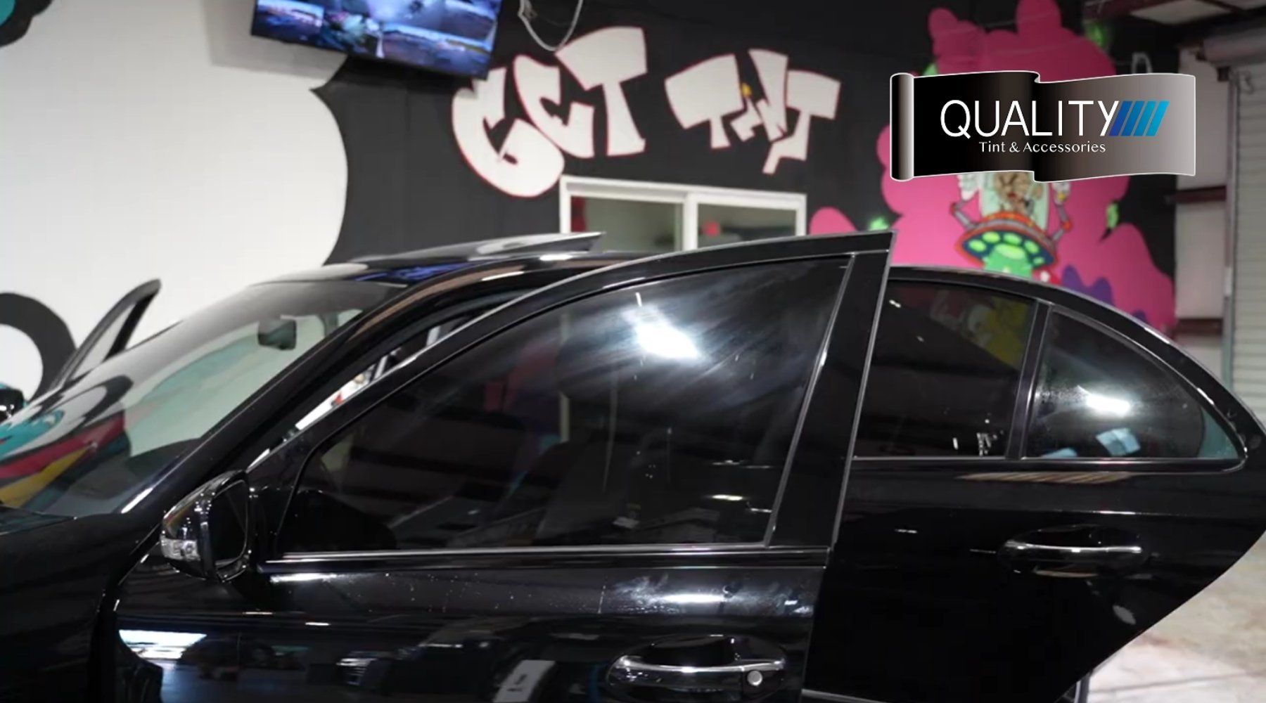 Black car with newly installed window tint inside a professional tinting shop.