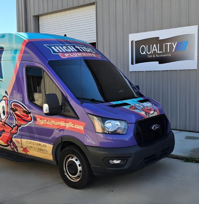 A vibrant High Tide Plumbing van with a cartoon crab graphic parked outside Quality Tint & Accessories in D'Iberville, MS. The building features signage for "QUALITY Tint & Accessories" and "LLumar Window Tinting" against a metal facade.