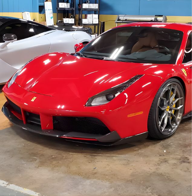 A vibrant red Ferrari 488 GTB and a sleek white McLaren 720S parked side by side inside a detailing shop at 1926 Bienville Blvd, Ocean Springs, Mississippi. The high-gloss finishes and custom wheels reflect the professional indoor lighting and clean garage floor.