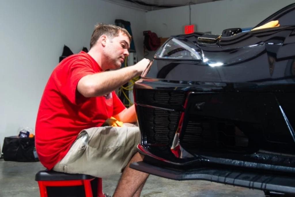 Technician applying ceramic coating to a black car’s front bumper, enhancing paint protection and delivering a high-gloss finish.
