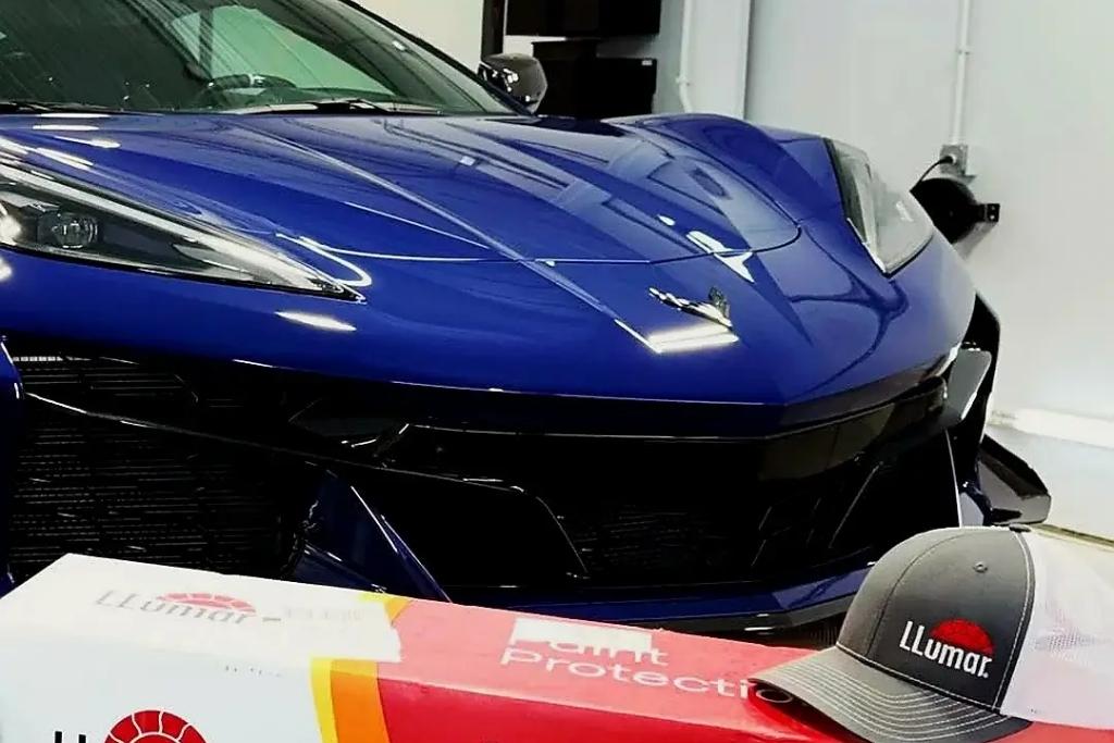 Blue Corvette prepared for professional ceramic coating with Llumar product display in foreground, emphasizing premium gloss and paint protection.