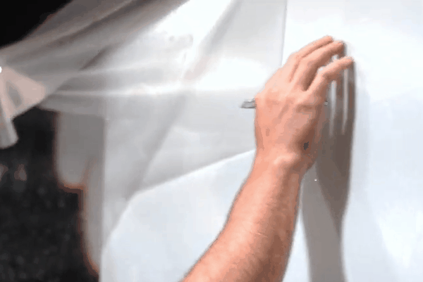 Close-up of a professional applying a transparent Paint Protection Film (PPF) to a vehicle’s surface using precision hand movements.