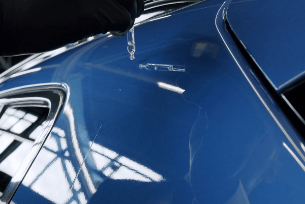 Close-up of ceramic coating being applied to a blue car surface using a precision dropper tool for enhanced paint protection and gloss.