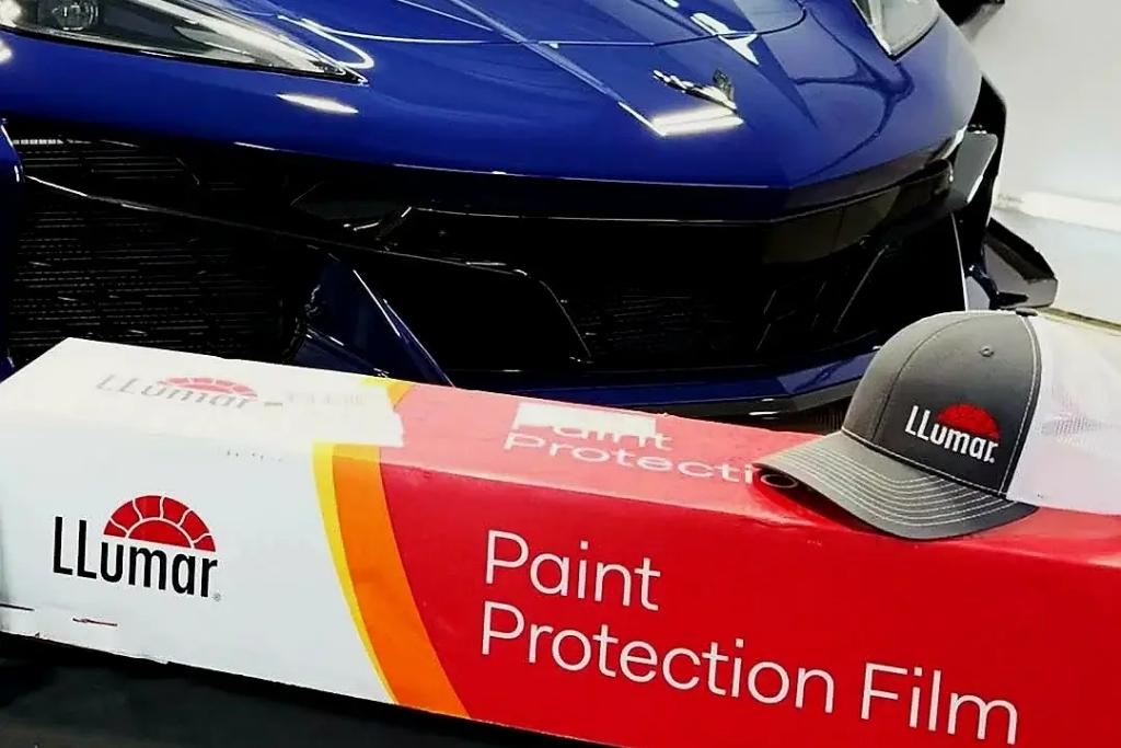 Box of LLumar Paint Protection Film and branded hat placed in front of a blue sports car.