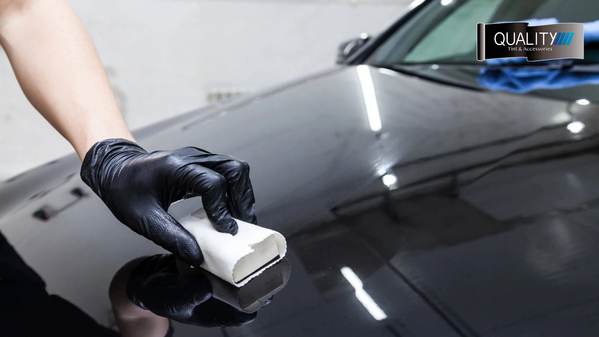 A gloved hand applies ceramic coating to the glossy black hood of a car using a white foam applicator.