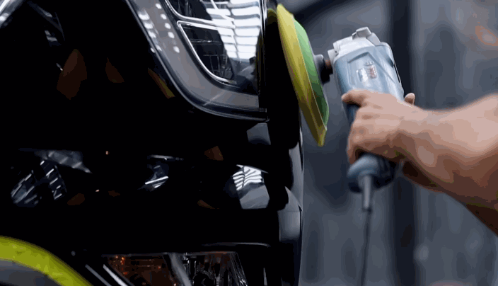 A technician uses a polishing machine with a green and yellow foam pad to buff the surface of a glossy black car, prepping it for ceramic coating.